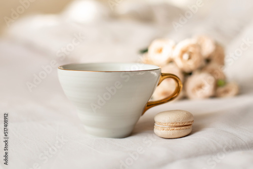 Sweet dessert, vanilla macaroons, mug and white roses on bed background. Romantic morning breakfast at bed.