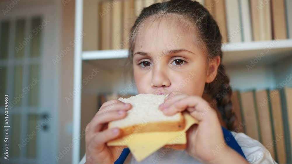 schoolgirl eats a sandwich at school during recess with backpack and bookcase. child lunch education concept. child in classroom having lunch snack with lifestyle bread and cheese sandwich schoolgirl eats a sandwich at school during recess with backpack and bookcase. child lunch education concept. child in classroom having lunch snack with lifestyle bread and cheese sandwich