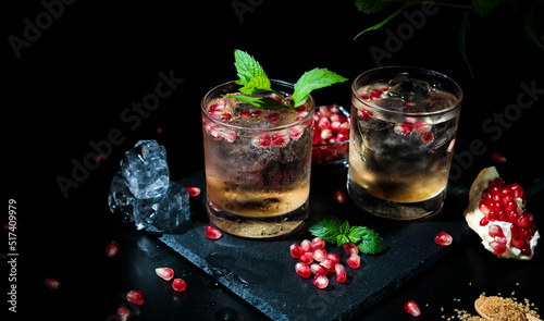 two colorful summer drinks with mint, pomegranate and ice cubes on a black background