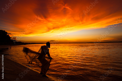 A Fisherman Catching in fish On Sea Against orange Sky During Sunset
