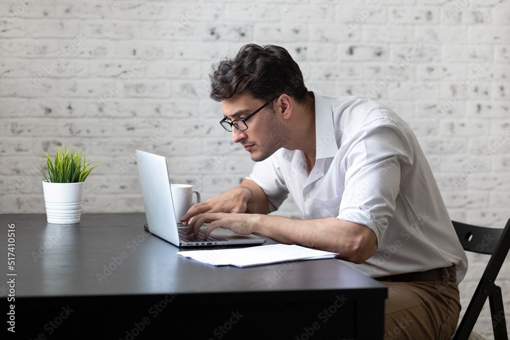 Handsome young businessman freelancer working on laptop at the desk in the living room. Distant work from home concept
