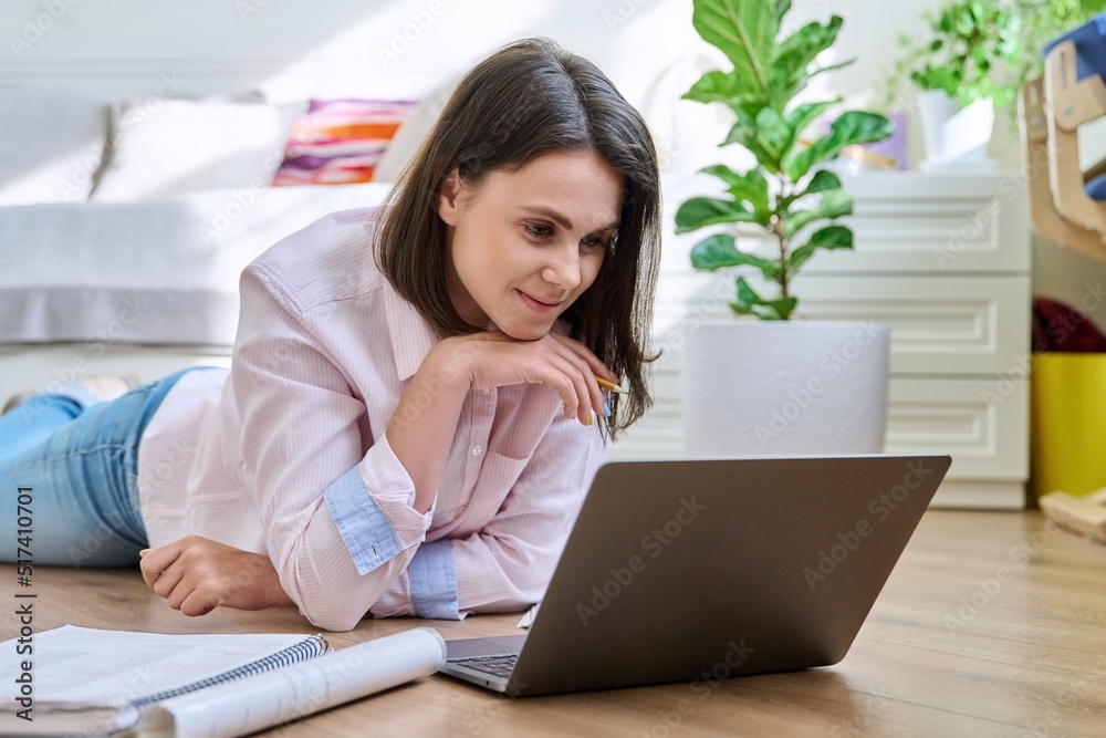 Young female university student studying at home lying on floor using laptop Young female university student studying at home lying on floor using laptop