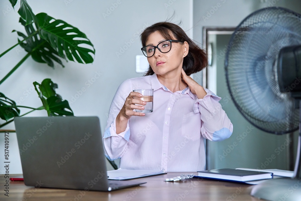 Middle aged Woman Suffering From Heat Overheated Cooled By Fan And middle-aged-woman-suffering-from-heat-overheated-cooled-by-fan-and