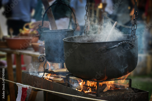 Large iron kettle or caldron with steaming stew over fire, food for all on a pristine outdoor feast, selected focus