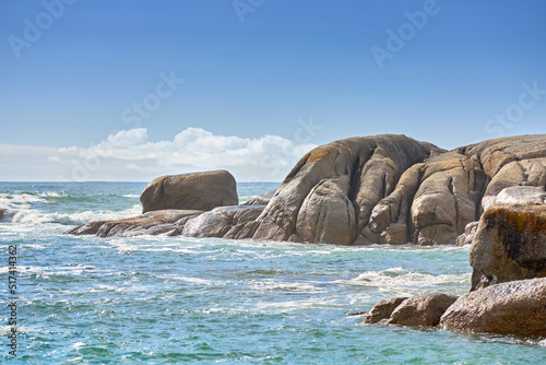 Copy space at sea with a cloudy blue sky background and rocky coast in Camps Bay, Cape Town, South Africa. Boulders at a beach shore across a majestic ocean. Scenic landscape for a summer holiday
