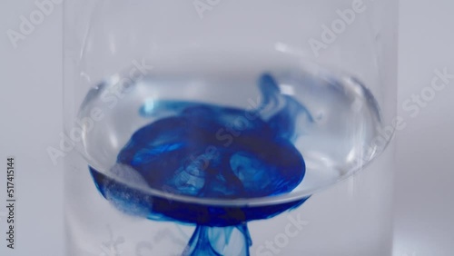 Dark blue drop is being adding to clear liquid in the flask. close-up of mixing bluecolored substance with transparent fluid in a glass bulb. photo