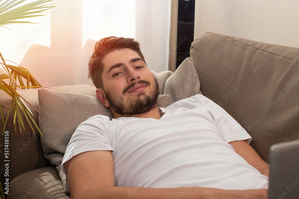 Jeune homme allongé dans son canapé qui utilise un ordinateur portable pour travailler, regarder un film ou faire des achats en ligne