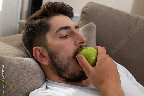 Fotografia gros plan sur le visage d'un jeune homme qui mange une pomme, allongé dans son c