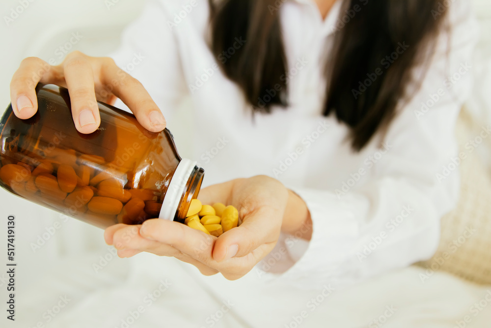 Sick woman sitting in bed pouring antibiotics to treat symptoms of