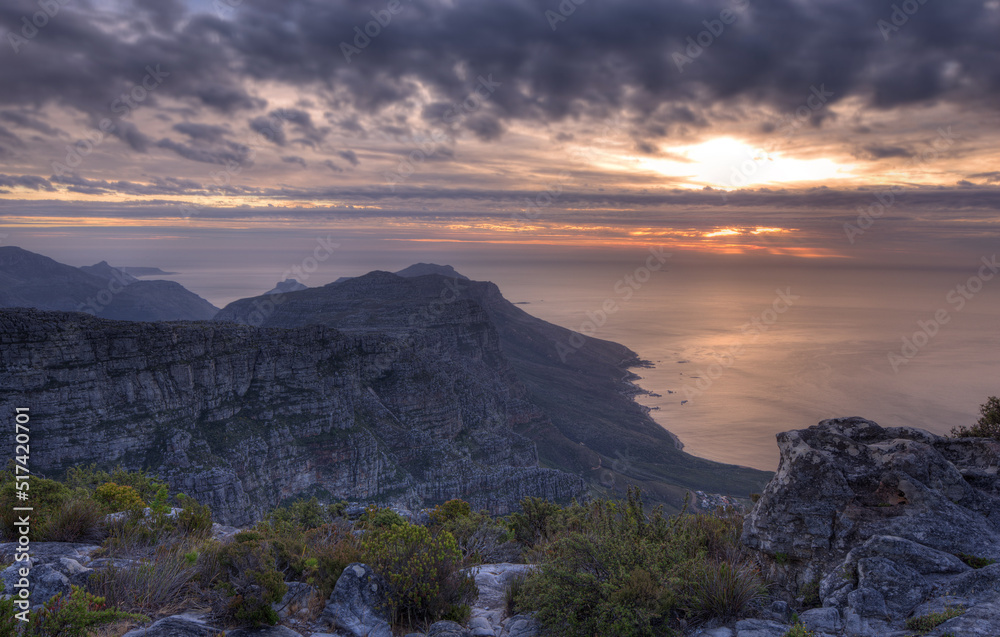 Above view of a mountain coastline at sunset in South Africa. Scenic landscape of dark clouds over a calm and peaceful ocean near Cape Town with the sun behind grey clouds in the sky and copy space