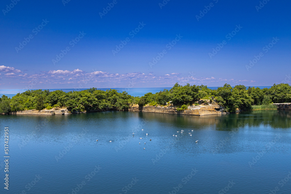 Scenic View of a Lake separated from Ocean by cliff rocky walls with trees grown on top of it all against a blue sky with purple clouds and some seagulls in the pond Scenic View of a Lake separated from Ocean by cliff rocky walls with trees grown on top of it all against a blue sky with purple clouds and some seagulls in the pond