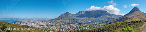 Panoramic landscape of Table mountain and surrounding urban town and a scenic road for traveling along Cape Town, South Africa. A mountain road overlooking the city with a cloudy blue sky in summer © SteenoWac/peopleimages.com