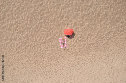Rapariga deitada na praia com guarda sol ao lado aberto e chapéu de palha a tapar a cabeça, vista aérea photo