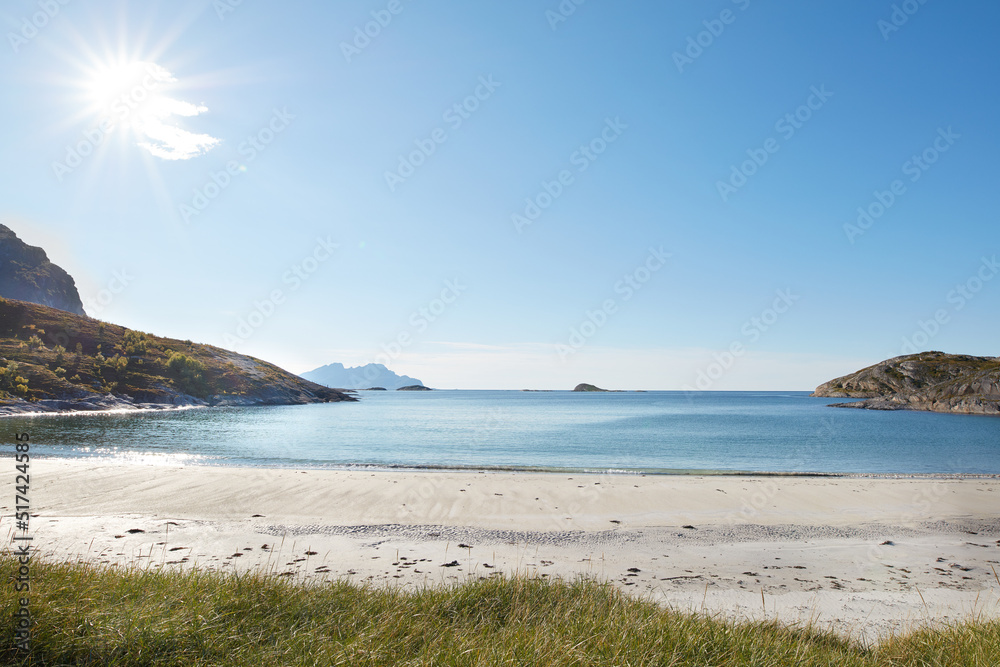 Copyspace at the beach with blue sky background above the horizon with lens flare. Calm ocean waves across an empty sea along the shore. Peaceful and tranquil landscape for a relaxing summer holiday