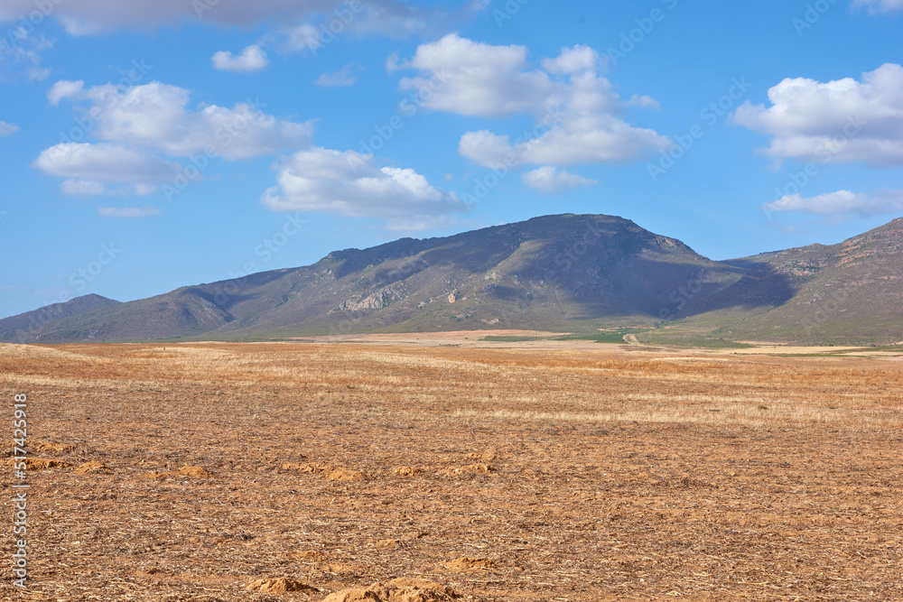 Farmland in the Western Cape of South Africa in the middle of the day. A mountain in a bare land with a cloudy blue sky. An empty farm with a nature view and a copy space. Farmland in the Western Cape of South Africa in the middle of the day. A mountain in a bare land with a cloudy blue sky. An empty farm with a nature view and a copy space.
