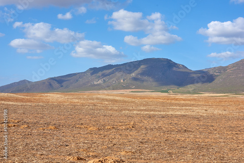 Farmland in the Western Cape of South Africa in the middle of the day. A mountain in a bare land with a cloudy blue sky. An empty farm with a nature view and a copy space.