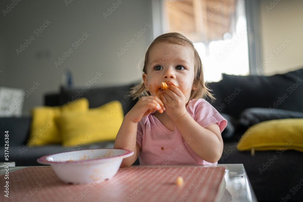 one girl small caucasian toddler female child daughter eating alone at the table at home while watching tv making mess on her face dirty sauce childhood growing up development concept copy space one girl small caucasian toddler female child daughter eating alone at the table at home while watching tv making mess on her face dirty sauce childhood growing up development concept copy space