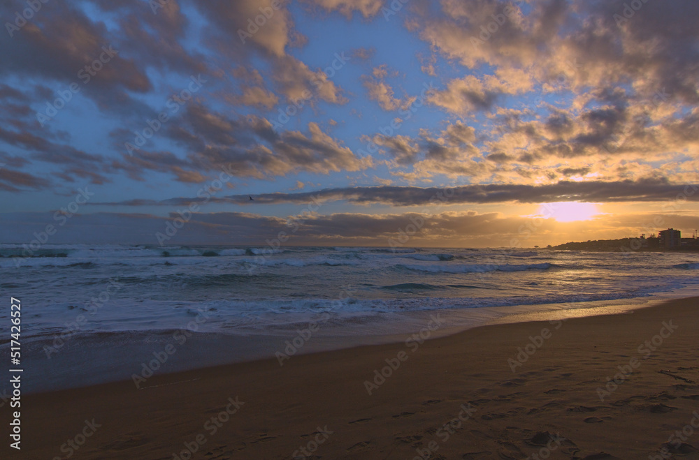 puesta de sol en la orilla de la playa con ciudad de fondo, lente gran angular