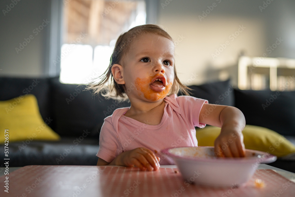 one girl small caucasian toddler female child daughter eating alone at the table at home while watching tv making mess on her face dirty sauce childhood growing up development concept copy space one girl small caucasian toddler female child daughter eating alone at the table at home while watching tv making mess on her face dirty sauce childhood growing up development concept copy space