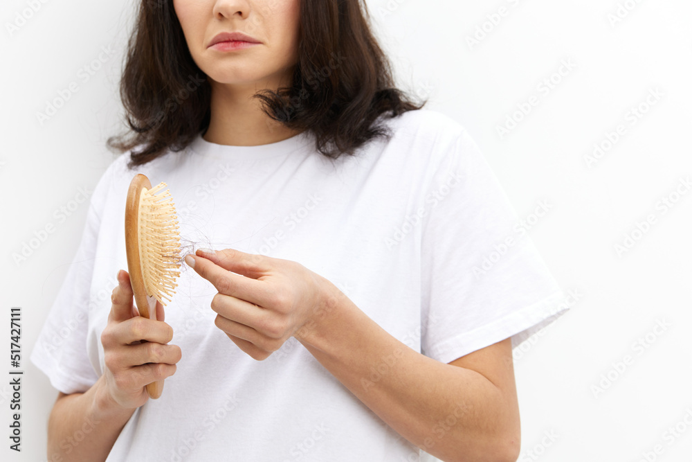 a close horizontal photo of a woman in a white T-shirt on a white background cleaning a comb from fallen hair, looking at the nh with the corners of her lips down a close horizontal photo of a woman in a white T-shirt on a white background cleaning a comb from fallen hair, looking at the nh with the corners of her lips down