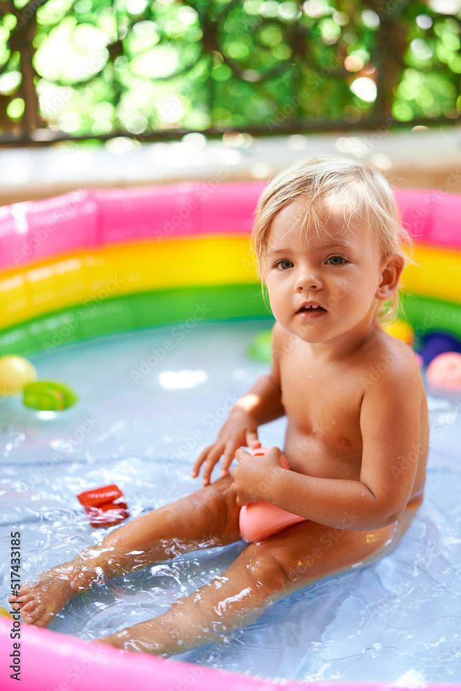 Little girl sits in an inflatable pool on the balcony with a toy