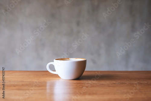 A white cup of hot coffee on wooden table with concrete wall background