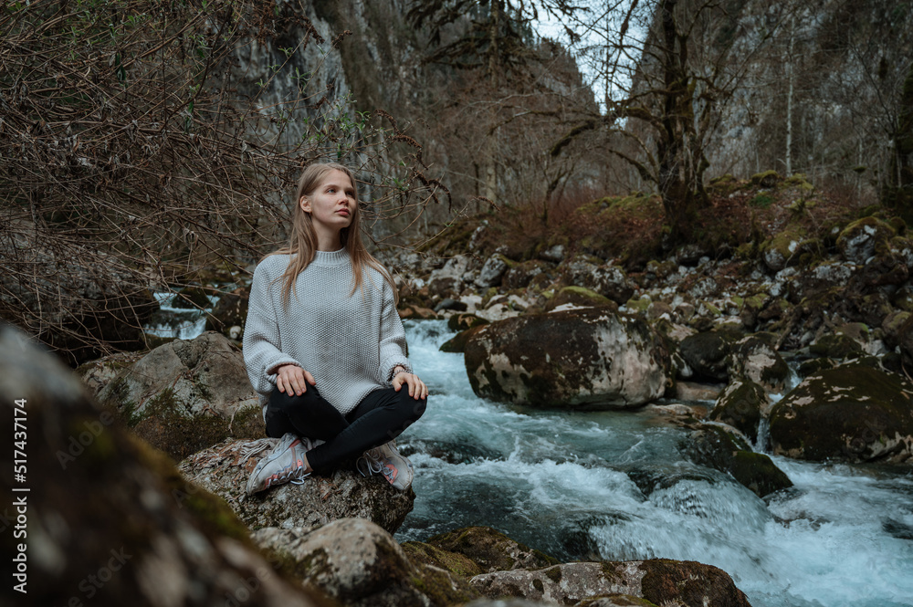 Girl sits on a large stone and meditates near a waterfall next to a mountain river. Girl sits on a large stone and meditates near a waterfall next to a mountain river.