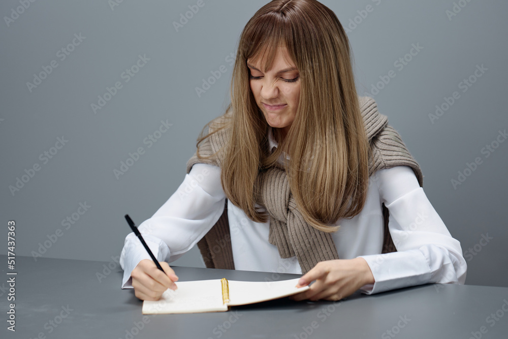 Angry irritated young blonde student lady freelancer in warm sweater hate doing home task at copybook in gray modern home office. Remote Job, Education And Career Profession Concept. Copy space Angry irritated young blonde student lady freelancer in warm sweater hate doing home task at copybook in gray modern home office. Remote Job, Education And Career Profession Concept. Copy space