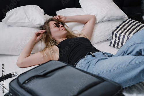 Woman with suitcase on bed in hotel having rest while traveling. Relaxed happy Traveler with bags in hostel Top view. Enjoying trip booking apartments. Arriving at resort
