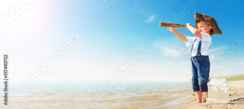 Kid play on the beach on a hot sunny day. Little girl dressed as a pirate stands barefoot on the sandy shore and launches a ship into the sea. Child dreaming of travel and adventure.