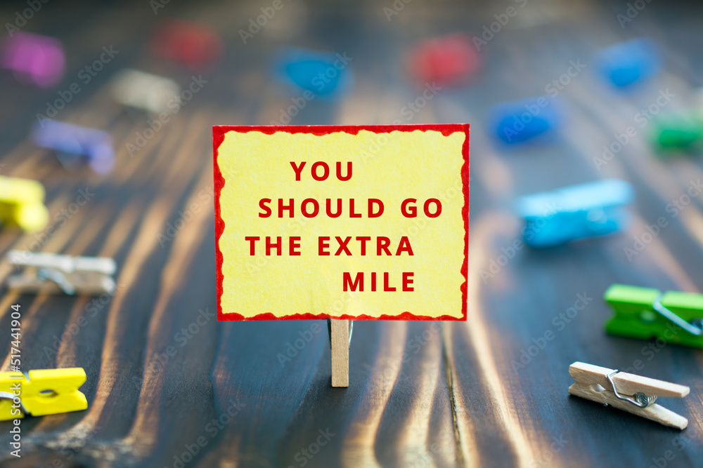 You should go the extra mile - phrase motivation concept, colored paper plate, wooden background, multicolored clothespins