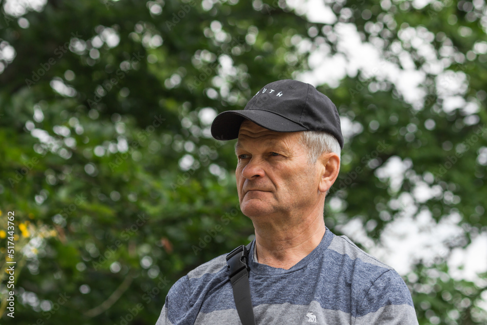 Portrait of serious caucasian senior man with black baseball cap and casual clothing. Isolated on the nature background.