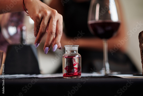Close-up image of sorceress adding blood in vial with magic love potion
