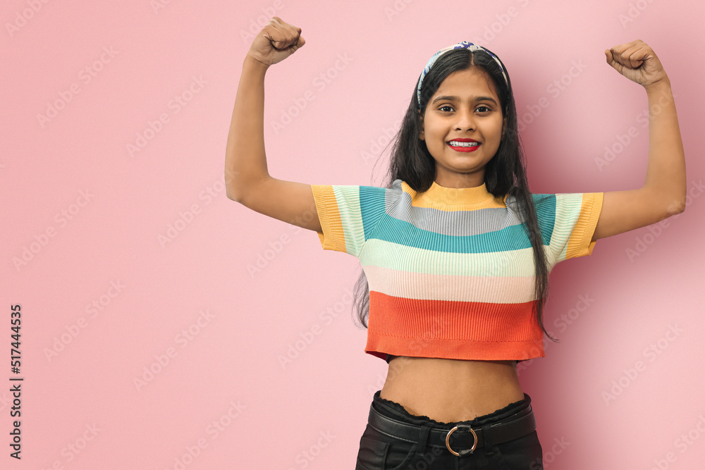 Strong powerful smiling cheerful Indian Asian girl posing isolated with toothy smile, raises arms and shows biceps. Look at my muscles! Mock up copy space