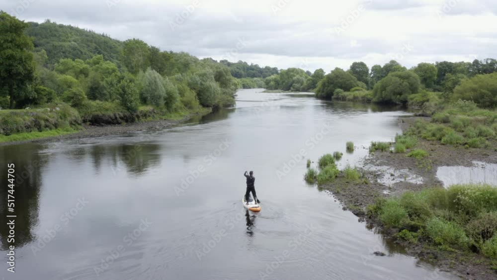 Lone man paddles SUP on small peaceful river in rural countryside Lone man paddles SUP on small peaceful river in rural countryside