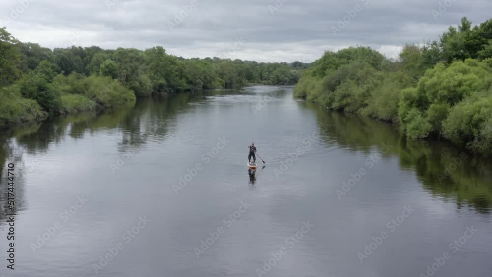Standup paddleboarder paddles toward camera on green country river Standup paddleboarder paddles toward camera on green country river