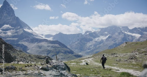 Black male traveler with backpack looking around cliffside exploring the mountain landscape near the Matterhorn in Switzerland photo