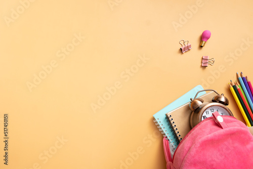 backpack with notepads and alarm clock with teddy bear and colorful pensils on colored background with copy space. Back to school concept