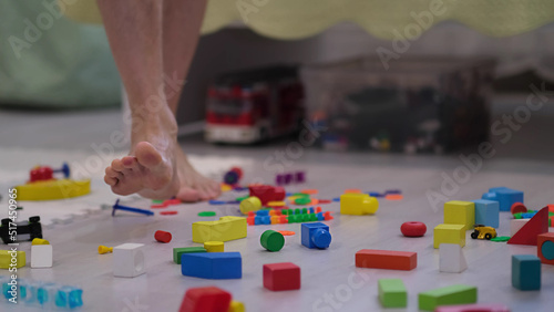 barefoot man walks among the scattered toys. Foot stepping on children's toys. Scattered toys on the floor. concept of an abundance of toys in the modern world.