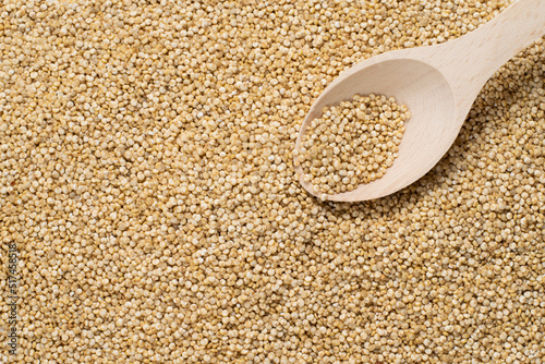 Grains of uncooked white quinoa and a wooden spoon with seeds on it. Top view, space for text, copy space, quinoa grains as texture, background.