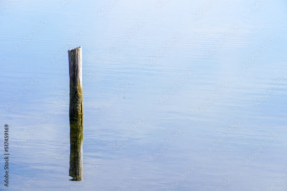A beautiful shot of a calm seascape with a broken pillar sticking out of the water on the horizon background.
