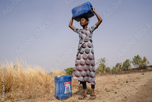 Young African girl with water containers looking into the distance, estimating the long walk to the village tap