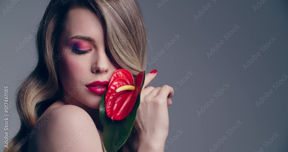 Sexy blonde woman with red lips holds a red flower. Fashion model with a long wavy hair posing at studio. Closeup face of a pretty young woman with bright makeup. Slow motion. Sexy blonde woman with red lips holds a red flower. Fashion model with a long wavy hair posing at studio. Closeup face of a pretty young woman with bright makeup. Slow motion.