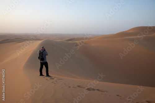 Man with a camera and backpack in desert at sunrise.