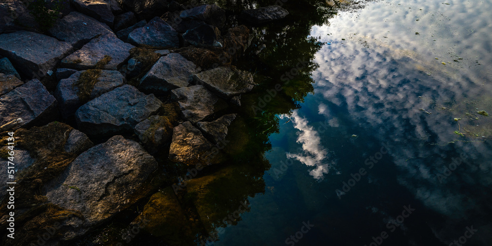 Abstract geometry of riverbank rocks and cloud reflections in the water at Big Stone Lake animal sanctuary in Minnesota, USA.