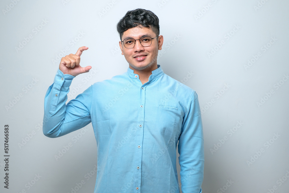 Fototapeta premium Young handsome man smiling and confident gesturing with hand doing small size sign with fingers looking and the camera. measure concept.