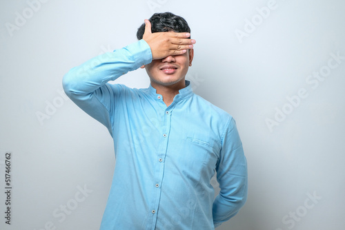 Young handsome asian man covering one eye with hand, confident smile on face and surprise emotion.