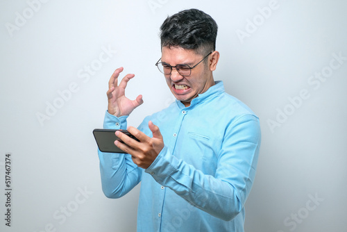 Angry Asian young man in casual shirt using mobile phone playing game