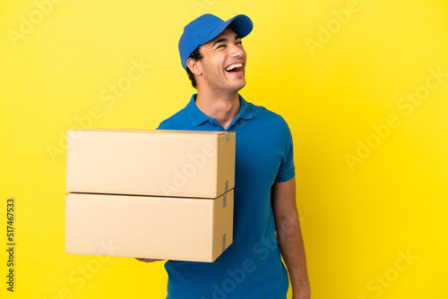 Delivery man over isolated yellow wall laughing