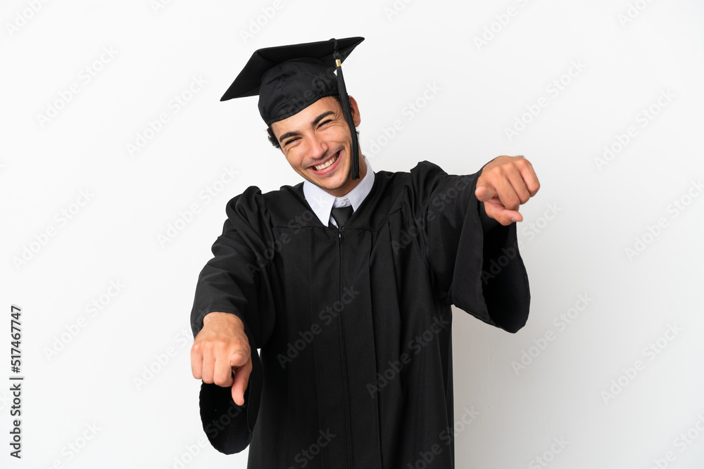 Young university graduate over isolated white background points finger at you while smiling Young university graduate over isolated white background points finger at you while smiling
